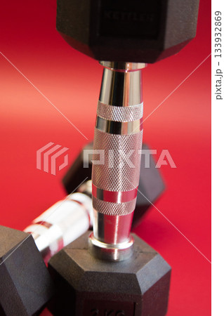 A detailed view of black dumbbells with metallic grips, arranged on a bright red surface, emphasizing strength training and fitness lifestyle choices A detailed view of black dumbbells with metallic grips, arranged on a bright red surface, emphasizing strength training and fitness lifestyle choices 133932869