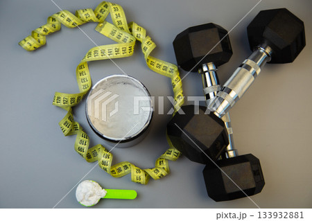 Fitness gear featuring dumbbells, measuring tape, and protein powder container on a gray background, illustrating healthy lifestyle and workout essentials Fitness gear featuring dumbbells, measuring tape, and protein powder container on a gray background, illustrating healthy lifestyle and workout essentials 133932881