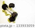 Dumbbells placed on a clean white background, intertwined with a yellow measuring tape, representing fitness, health, and the journey towards personal training success 133933059