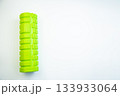 Vibrant green foam roller placed on a white background, highlighting its unique texture and shape, ideal for muscle recovery and fitness routines 133933064