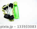 Fitness gear featuring black dumbbells, a vibrant green water bottle, and a measuring tape on a bright white background, representing a healthy lifestyle and exercise motivation 133933083