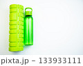 Green fitness foam roller and water bottle placed on a bright white surface, emphasizing wellness and exercise, perfect for active individuals and fitness routines 133933111