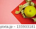 A yellow apple is artistically placed with a measuring tape on a colorful geometric background, representing themes of health, wellness, and nutrition in a creative setting 133933181
