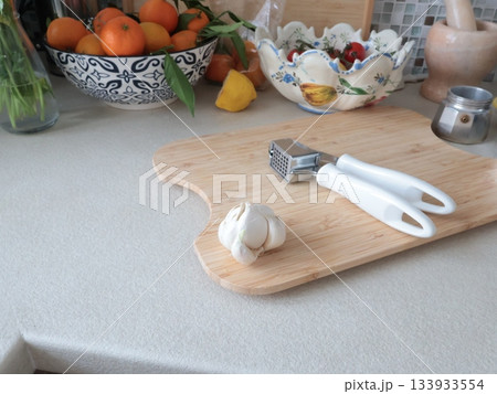 Garlic press on wooden cutting board in kitchen on table. Vintage tableware, traditional objects. Europe, Mediterranean diet, healthy eating. 133933554