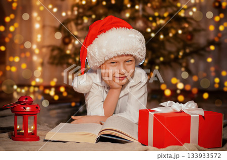 child in Santa Claus hat on Christmas tree background with gift and book child in Santa Claus hat on Christmas tree background with gift and book 133933572
