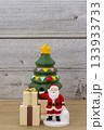 クリスマスツリーとプレゼントの箱の横に立つサンタクロースのミニチュア（木目調の背景） 133933733