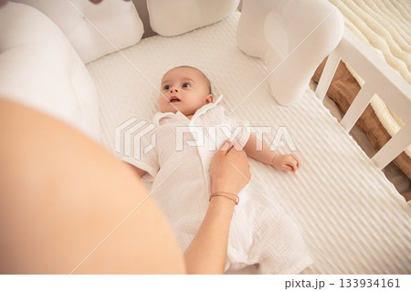 A mother gently interacts with her baby in a crib 133934161