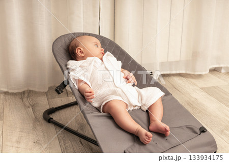 Baby enjoys a peaceful moment in a cozy bouncer at home 133934175