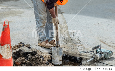 A plumber working on the street road opening asphalt using special equipment. A plumber working on the street road opening asphalt using special equipment. 133935043
