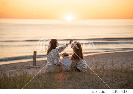Back view of two caucasian female friends and a child enjoying sunset on the Baltic seashore. Back view of two caucasian female friends and a child enjoying sunset on the Baltic seashore. 133935383