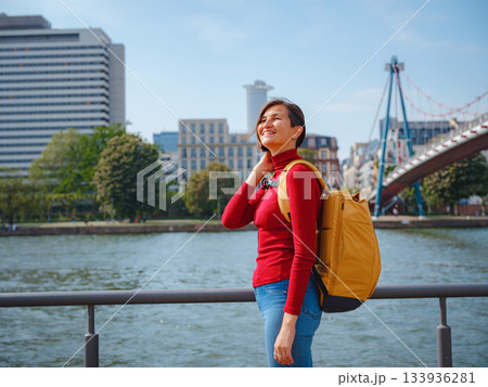 Tourist woman explores modern Frankfurt, walking through vibrant streets with contemporary architecture, skyscrapers, and urban spaces, enjoying lively atmosphere of modern side. 133936281