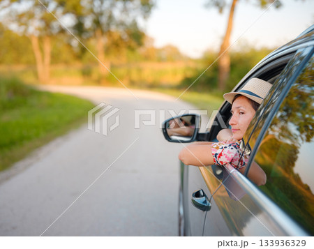 Traveler woman in red ethnic dress and hat drives car through scenic countryside of Croatia in summer. Surrounded by lush fields and forests, she enjoys peaceful and adventurous road trip Traveler woman in red ethnic dress and hat drives car through scenic countryside of Croatia in summer. Surrounded by lush fields and forests, she enjoys peaceful and adventurous road trip 133936329