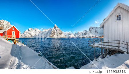 Traditional Norwegian  houses on the shore of  Reinefjorden on Toppoya island and snowy mountaines in background 133938218