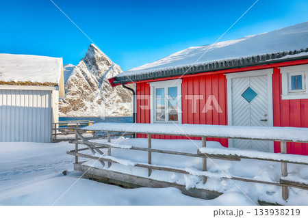 Traditional Norwegian  houses on the shore of  Reinefjorden on Toppoya island and snowy mountaines in background 133938219