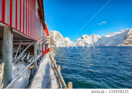 Traditional Norwegian  houses on the shore of  Reinefjorden on Toppoya island and snowy mountaines in background 133938225