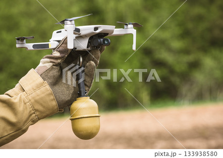 Operator in military colored clothes holds in hand preparing a drone for flight attached grenade Operator in military colored clothes holds in hand preparing a drone for flight attached grenade 133938580