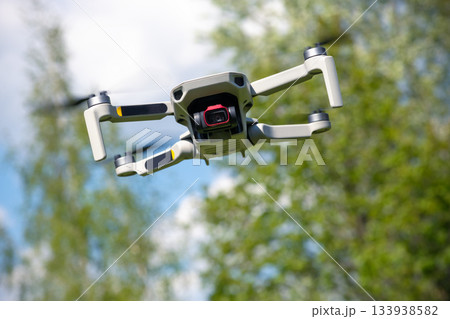 Small Flying Qunmanned aerial vehicle in flight mode with camera outdoor on sunny day summer time blue green garden background Small Flying Qunmanned aerial vehicle in flight mode with camera outdoor on sunny day summer time blue green garden background 133938582