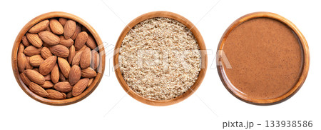 Whole almonds, ground, and almond butter, in wooden bowls. From left to right dried almonds with skin, ground unpeeled almonds, and processed into a paste. Prunus dulcis. Isolated, from above. Photo 133938586