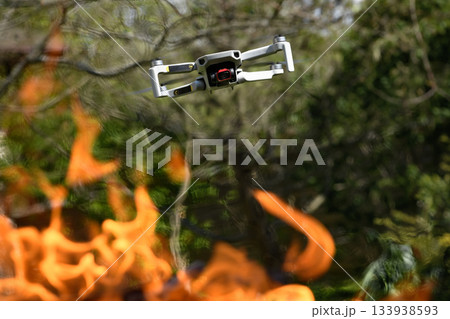 Flying drone Quadcopter with camera pointed at viewer outdoor in a fire in the foreground spurts of flame forest background Flying drone Quadcopter with camera pointed at viewer outdoor in a fire in the foreground spurts of flame forest background 133938593