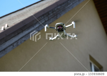 Drone in the air inspecting the roof over the house closeup blue sky background 133938609