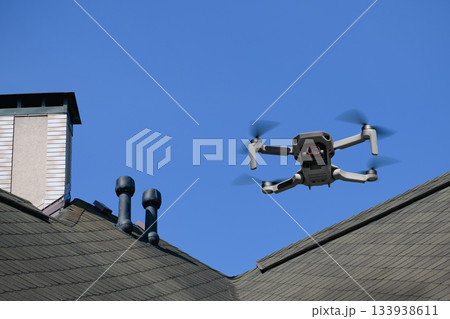 Drone in the air inspecting the roof over the house closeup on blue sky background 133938611