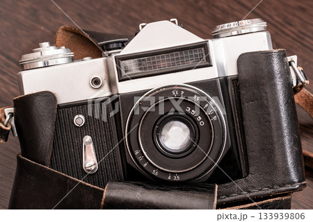 The Classic Vintage Old shabby Photo Camera in a dark brown case open lens brown natural leather Strap on  Wooden table 133939806