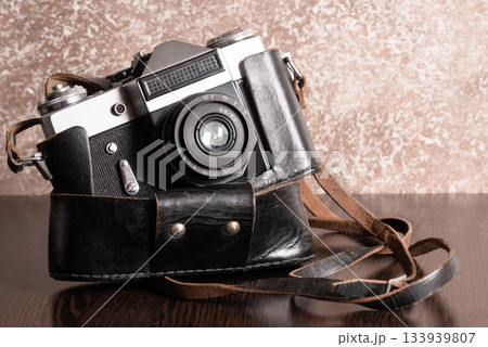 The Classic Vintage Old shabby Photo Camera in a dark brown case open lens brown natural leather Strap on Wooden table The Classic Vintage Old shabby Photo Camera in a dark brown case open lens brown natural leather Strap on Wooden table 133939807