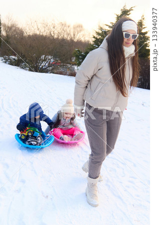 Woman pulling children on sleds in snowy weather during the daytime 133940377