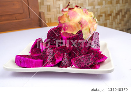Sliced vibrant dragon fruit on white plate with whole fruit 133940579
