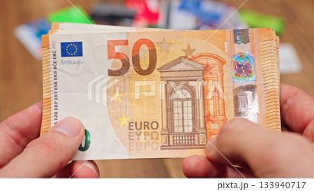 Man holding US hundred dollar bills with both hands, blurred credit cards on a table in the background, representing finances, spending, and cash management. Man holding US hundred dollar bills with both hands, blurred credit cards on a table in the background, representing finances, spending, and cash management. 133940717