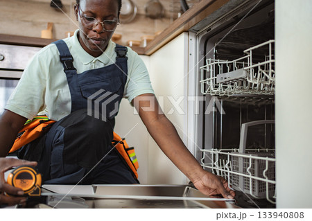 Technician taking measurements for dishwasher installation in kitchen 133940808
