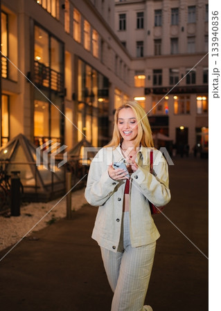 Woman smiling using smartphone walking city street at night in V 133940836