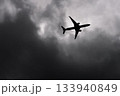 Large passenger airplane airliner silhouette flying in the cloudy sky bottom view dark grey clouds 133940849