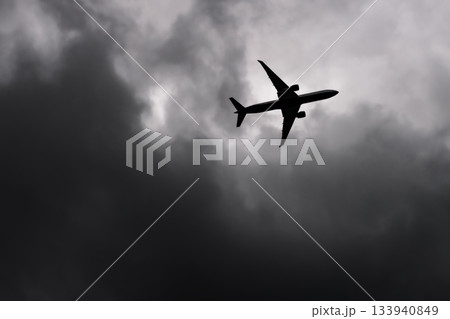 Large passenger airplane airliner silhouette flying in the cloudy sky bottom view dark grey clouds 133940849