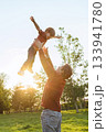 Father tossing his smiling young son into the air while playing outdoors 133941780