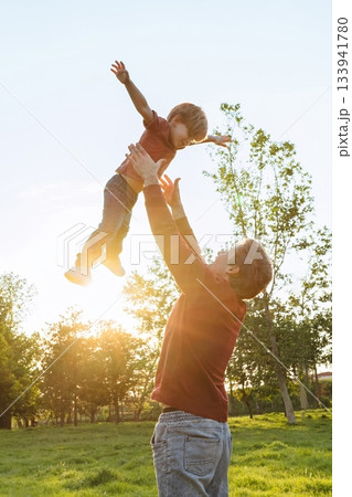 Father tossing his smiling young son into the air while playing outdoors 133941780