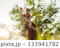 A happy dad carries his smiling son on his shoulders in a park at sunset 133941782