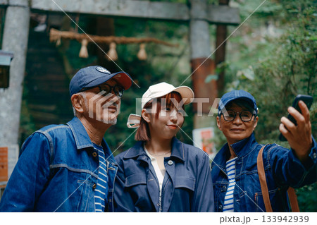 神社の鳥居前で親子3人がスマホで自撮りする家族旅行シーン 133942939