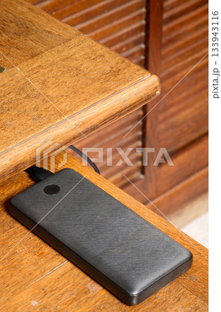 Indoor. power bank placed on the corner of a wooden desk Indoor. power bank placed on the corner of a wooden desk 133943116