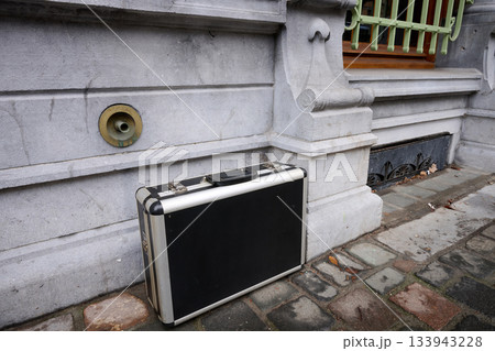 Outdoor. an old suitcase at the edge of a wall of a period-style house 133943228