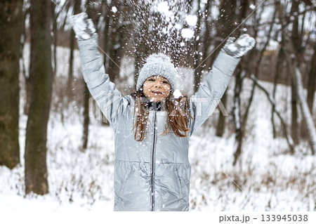 Girl in gray winter coat and knit hat throws snow in a snowy forest Girl in gray winter coat and knit hat throws snow in a snowy forest 133945038