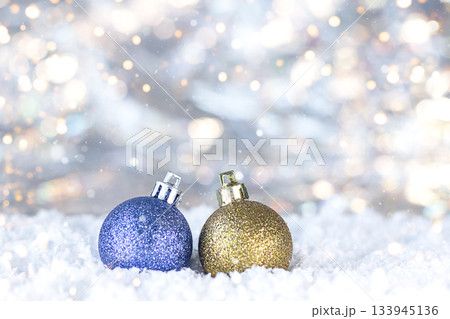 Glitter blue and gold ornaments on snow under festive bokeh glow for holiday decor Glitter blue and gold ornaments on snow under festive bokeh glow for holiday decor 133945136