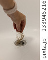 Water drain hole is clogged with hair clump. Woman hand is cleaning the bathroom sewer trap. Close-up.  133945216
