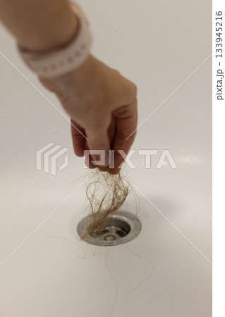 Water drain hole is clogged with hair clump. Woman hand is cleaning the bathroom sewer trap. Close-up. Water drain hole is clogged with hair clump. Woman hand is cleaning the bathroom sewer trap. Close-up. 133945216