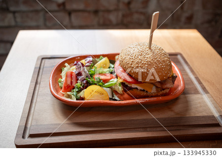 Delicious gourmet burger served with fresh vegetables on a wooden table Delicious gourmet burger served with fresh vegetables on a wooden table 133945330