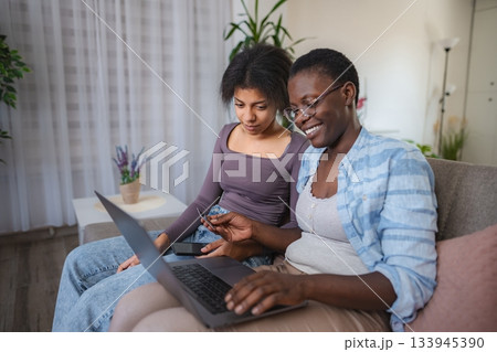 Two African American women shopping online using laptop and credit card at home Two African American women shopping online using laptop and credit card at home 133945390