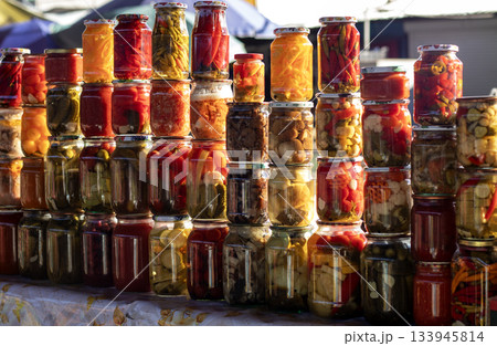 Colorful jars of pickled vegetables on a market stall under bright sunlight 133945814