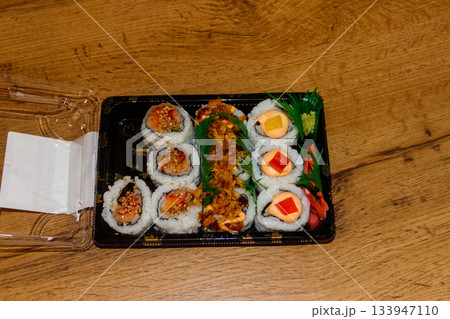 Set of sushi rolls in plastic box on wooden table. Sushi for take away or delivery of sushi in plastic container Set of sushi rolls in plastic box on wooden table. Sushi for take away or delivery of sushi in plastic container 133947110
