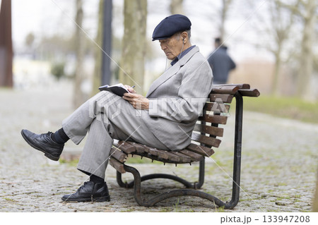 Elderly writer taking notes in notebook while sitting on park bench Elderly writer taking notes in notebook while sitting on park bench 133947208