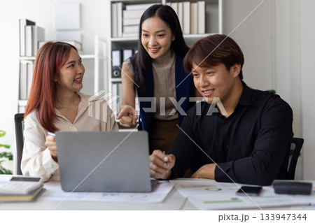 Asian businesspeople are collaborating on a project, analyzing data on a laptop and discussing strategies in office, working together to achieve their business goals. 133947344